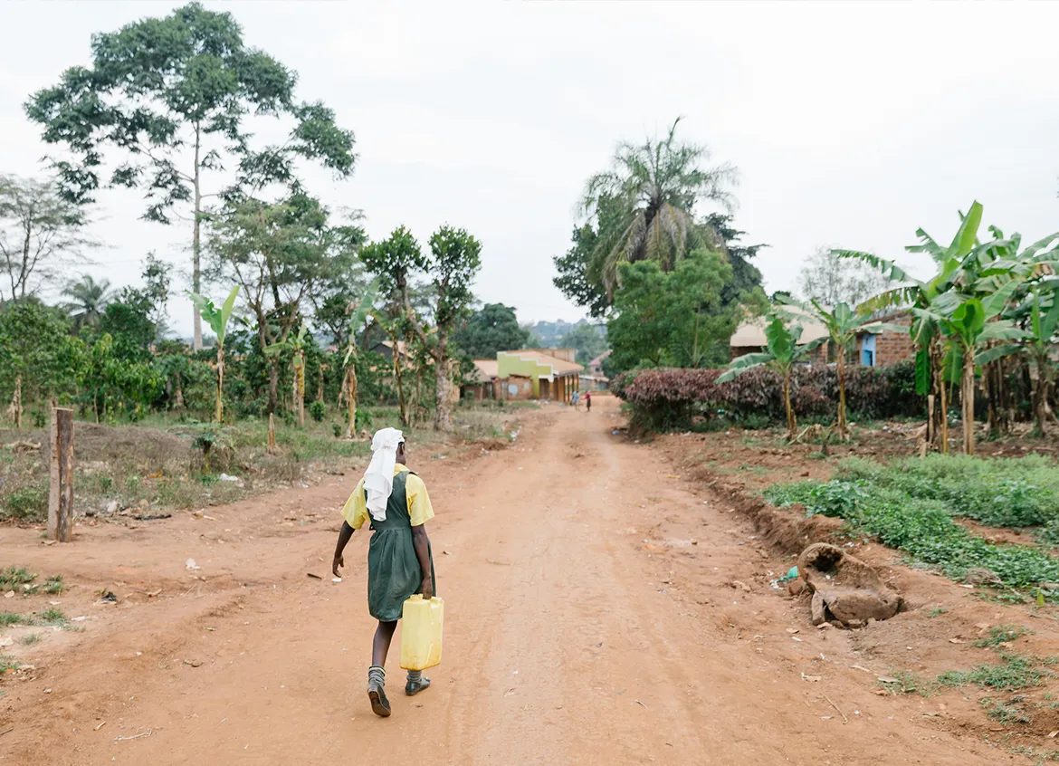 Young woman in a school uniform walking to retrieve water carrying a yellow vessel.